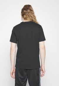 T-shirt en coton noir avec un col rond et des manches courtes, présenté de dos. Texture lisse, design simple et surface sans ornements.