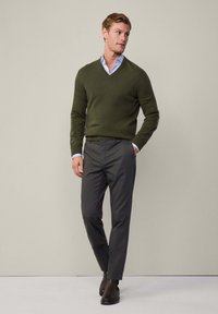 Men's olive green v-neck sweater, tailored dark gray trousers, and brown leather ankle boots. Smooth texture, fitted design, and subtle accents.