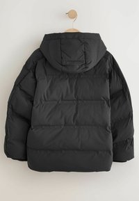Schwarz, gepolsterte Jacke mit Kapuze und gestepptem Design, mit weicher Textur und sichtbaren Nähten entlang der Seiten, hängt an einem Holzkleiderbügel.