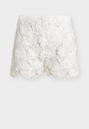 Shorts en dentelle blanche avec motifs floraux et ourlet festonné, présentant une broderie florale 3D complexe et un design délicat texturé.