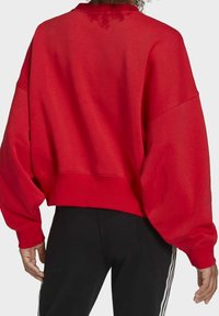 Rode cropped sweatshirt met oversized mouwen en geribbelde zoom. De stof lijkt zacht; de achterkant toont een lichte textuurvariatie bij de halslijn.