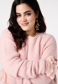 Pull rose pâle duveteux à manches longues avec des accents en dentelle aux poignets. Coulissé dans un détail en dentelle froncé à l'ourlet.