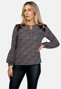 Czarna bluzka z białym kwiatowym wzorem, dekoltem w kształcie łezki i koronkowymi akcentami na ramionach. Długie rękawy z marszczonymi mankietami. Gładka tekstura materiału.