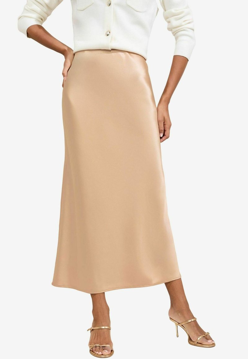 Satin midi krilo v svetli bež barvi, s gladko teksturo in ravno silhueto. V kombinaciji z zlatimi sandali na peto.