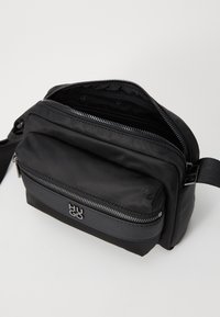 Sort nylon skuldertaske med en tekstureret overflade, lynlåslomme foran og logoaccent. Kompakt rektangulær form med justerbar rem.