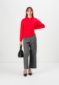 Sarkans kapucīnas krekls, pelēkas cargos bikses ar kabatām, melnas augstpapēžu kurpes un neliela melna somiņa. Vienkārša, ikdienišķa apģērba kompozīcija ar kontrastu.