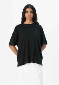 Sort oversized t-shirt i cotton med rund halsudskæring og korte ærmer. Har et lille broderet hjerte på venstre brystområde.