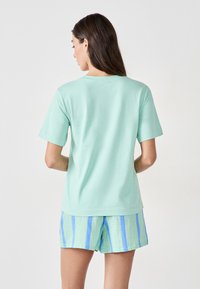 T-shirt in cotone verde menta con maniche corte e scollatura rotonda; abbinato a pantaloni corti verde chiaro con strisce verticali blu.