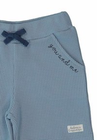 Blå byxor med våffeltextur och en marinblå fluga samt broderad text "du och jag" på fickan. Har en märkesetikett på nederkanten.