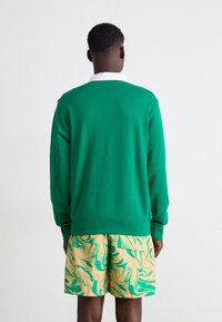 Grön sweatshirt med rund halsringning, lös passform och ribbade ärmslut. Kombinerad med gula shorts med ett grönt marmormönster.