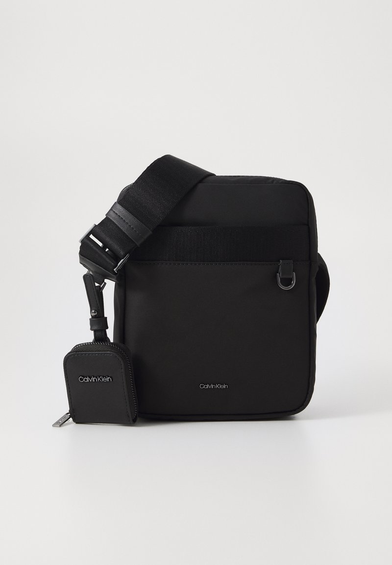 Borsa a tracolla nera in nylon, dotata di una piccola tasca staccabile, tracolla regolabile e dettagli con logo sia sulla borsa che sulla tasca.