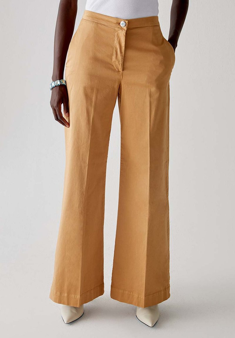 Pantaloni a gamba larga in cotone color beige chiaro, con chiusura anteriore a bottone e tasche laterali. Tessuto liscio con taglio pulito.