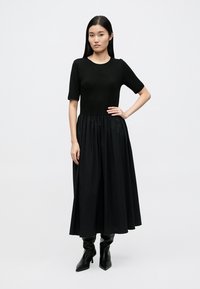 Vestido midi preto com parte superior justa de mangas curtas e saia volumosa. O material parece liso com um brilho subtil.