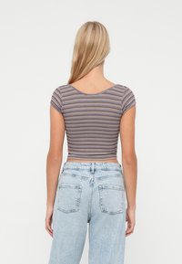 Kvinne med langt blondt hår som har på seg en kortermet stripete crop-top og lys blå høytlivsjeans, vender bort fra kameraet.
