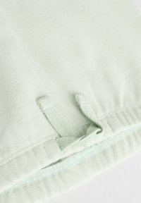 Tissu vert clair avec une texture douce, doté d'un cordon avec une boucle et d'un ourlet cousu. Design simple et finition lisse.