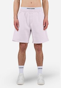 Ροζ ανοιχτόχρωμο σορτς φούτερ με ελαστική μέση, πλευρικές τσέπες και λεπτομέρειες με λογότυπο στη μέση. Φορεμένο με λευκές κάλτσες και παπούτσια.