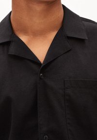 Czarna koszula z krótkim rękawem i kołnierzykiem, z zapięciem na guziki oraz kieszenią na piersi. Wykonana z teksturowanej tkaniny.