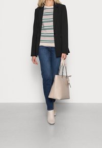Schwarzer taillierter Blazer über einem gestreiften Strickpullover, blaue Jeans und beigen Ankle Boots. Eine hellbeige Handtasche mit Kettenakzenten wird gehalten.