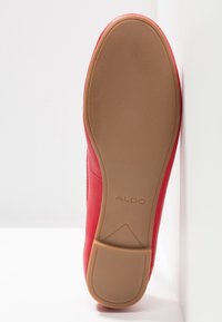 Chaussure rouge avec une texture lisse, un bout arrondi et une semelle en caoutchouc beige. La marque "ALDO" est visible sur la semelle.