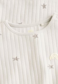 Soft white ribbed baby clothing with small gray stars and a cream-colored rainbow patch near the neckline.