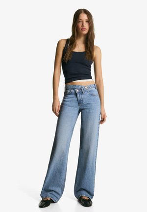 Jasnoniebieskie jeansy o szerokich nogawkach z wysokim stanem, z szlufkami na pasek i zapięciem na guzik, w połączeniu z dopasowanym granatowym topem na ramiączkach.