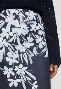 Jupe à motif floral avec un fond bleu marine orné de grandes fleurs blanches et bleu pâle. Tissu lisse avec un léger éclat.