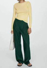 Haut à manches longues en maille côtelée jaune associé à un pantalon large à rayures fines vertes. Sac à main de couleur claire et sandales avec des lanières noires.