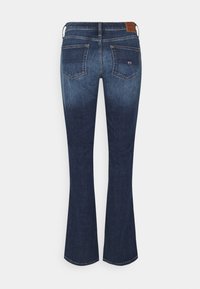 Uitlopende donkerblauwe spijkerbroeken hebben een gladde textuur, twee achterzakken en een logo-label op de tailleband.