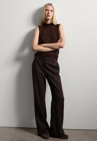 Haut sans manches marron associé à un pantalon large taille haute marron. Tissu lisse créant une silhouette décontractée. Chaussures foncées complètent le look.