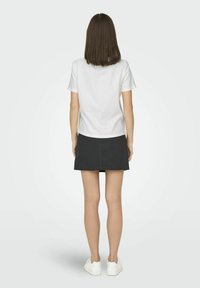 Hvid bomulds T-shirt med korte ærmer, parret med en sort miniskirt, der viser rene linjer og minimalistisk design. Båret med hvide sneakers.
