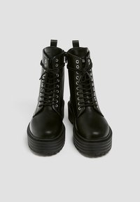 Bottes noires en cuir montant à la cheville, avec des semelles épaisses à plateforme rainurées. Elles sont dotées d'œillets métalliques, de lacets et de fermetures éclair latérales pour un enfilage facile.
