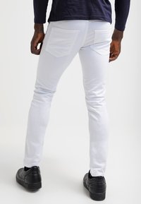 Bílé skinny džíny z denimu s kapsami na zadní straně, hladkým povrchem a kontrastním šitím, v kombinaci s černými nízkými sneakers.