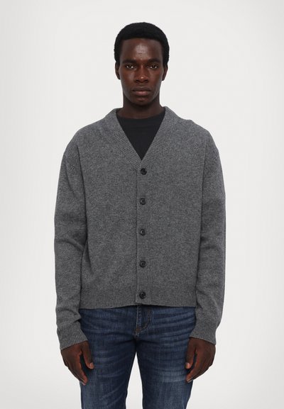 Cardigan gris avec un col châle, des poignets et un ourlet côtelés, comportant six boutons noirs sur le devant. Porté sur une chemise noire.