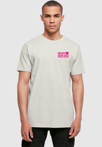 Grå kortærmet t-shirt lavet af bomuld, med et pink grafisk print på venstre bryst med teksten "MEIN ♥ SCHLÄGT SCHLAGER."