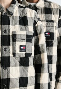 Juodas ir smėlinis laukinis raštas, suknelė su mygtukų uždarymu, krūtinės kišenė ir logotipo pleistras. Ypatumai: kontrastingas juodas siuvinėjimas ir mygtukų detalės.