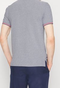 Grå polotröja med texturerad tyg, korta ärmar med röda och blå detaljer, samt rak nederkant. Buren över mörkblå shorts.