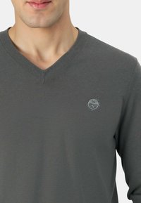 Maglione a V lavorato a maglia di colore grigio scuro, con trama a coste, silhouette aderente e piccolo logo circolare sul petto a sinistra.