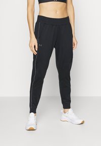 Svarta atletiska joggers med resårmidja, sidofickor och reflexdetaljer längs sömmarna, tillsammans med vita löparskor.