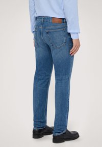 Tmavě modré džínové kalhoty, přiléhavý střih, s hnědým koženým páskem na zadní části, dvěma zadními kapsami a čistým lemem. Nosit s černými botami.