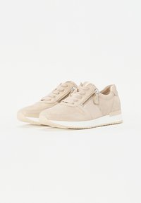 Baskets en suede beige avec une finition lisse, dotées d'une semelle en caoutchouc blanche, d'un laçage à l'avant et d'un détail à fermeture éclair sur le côté.