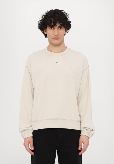 Felpa beige con collo girocollo, maniche raglan, polsini a coste e un branding discreto sul petto. Tessuto morbido con una vestibilità rilassata.