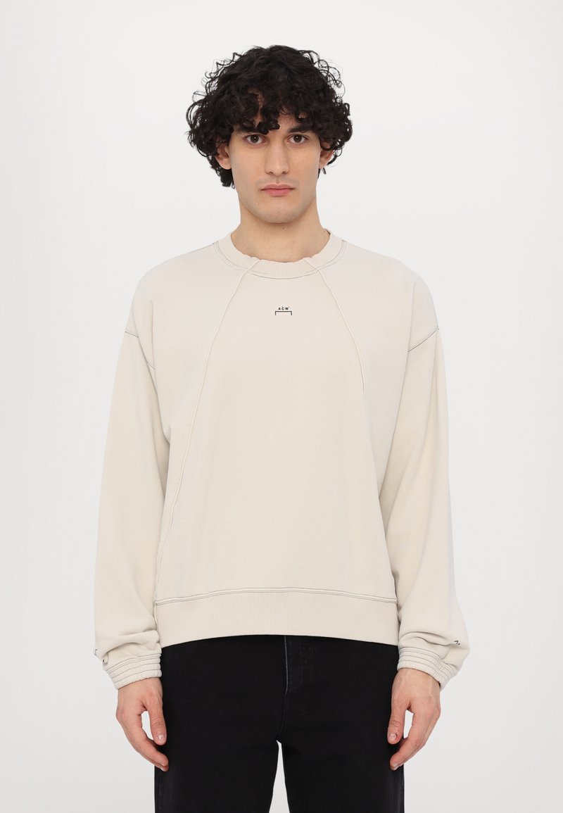 Sweatshirt beige avec un col rond, des manches raglan, des poignets côtelés et une discrète marque sur la poitrine. Tissu doux avec une coupe décontractée.