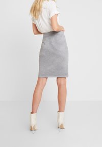 Jupe tricotée côtelée grise avec une silhouette ajustée, présentant une taille haute. Assortie à des bottines blanches à bout pointu.