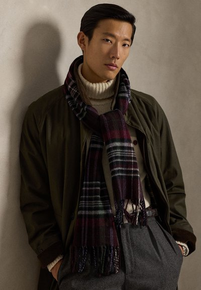 Vilnonis šalikas tamsaus languoto rašto su burgundiško, žalio ir juodo atspalviais. Dėvimas ant kreminės golfuko ir alyvuogių žalios spalvos paltuko.