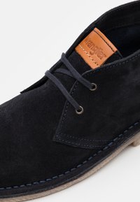 Scarpa in suede nera con un design a profilo basso, con accenti in pelle e cuciture blu, completata da occhielli e lacci in metallo.