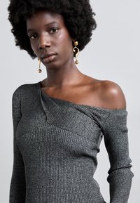 Γκρι ριμπ μπλούζα εκτός ώμου με μακριά μανίκια, που διαθέτει υφή. Συνοδεύεται από χρυσά σκουλαρίκια σε σχήμα ερωτηματικού.