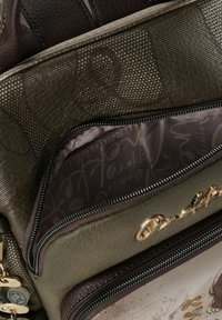 Braune Ledertasche mit strukturierten Mustern, ausgestattet mit einem Reißverschlussfach in Olivgrün und einem detaillierten Innenfutter. Goldfarbene Metallakzente.