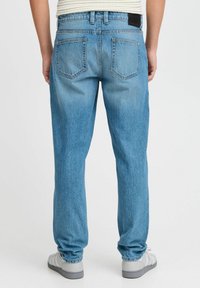 Jeans de denim azul claro con un corte recto, que cuentan con dos bolsillos traseros y una etiqueta negra en la cintura. Tejido texturizado con desgastes.