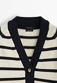 Cardigan tricoté avec des rayures horizontales noires et blanches, col côtelé noir, et un bouton décoratif unique à l'avant.
