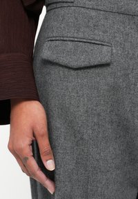 Pantalones de lana grises con un acabado texturizado, que cuentan con un bolsillo trasero y una mano reposando sobre la tela, mostrando una piel suave.